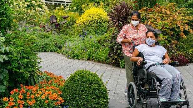 A woman in a wheelchair with another standing behind her at the New York Botanical Garden in NYC.
