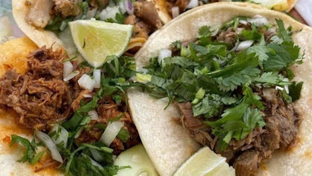 Close up of two tacos with meat, lettuce, cilantro, and lime