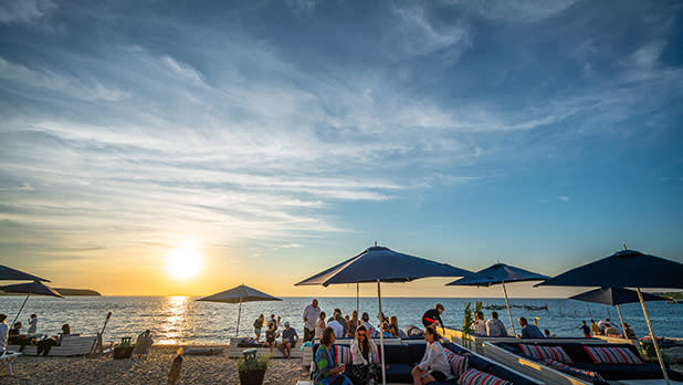People lounge on the beach under umbrellas during sunset at Navy Beach