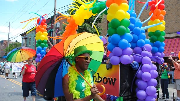 Man holding a rainbow flag and walking past rainbow-colored balloons and decorations.