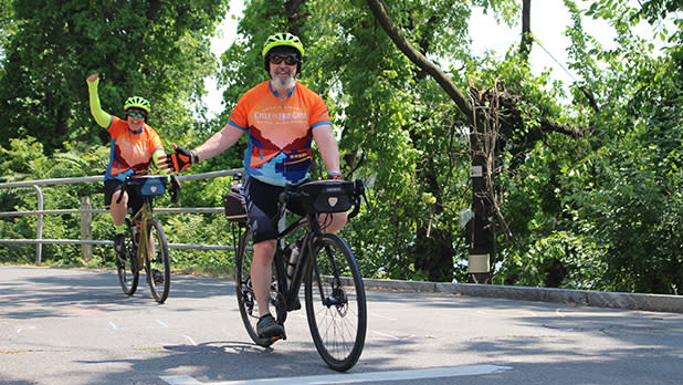 Two people wearing orange shirts and lime green helmets riding bikes on the Cycle the Erie Canal tour.