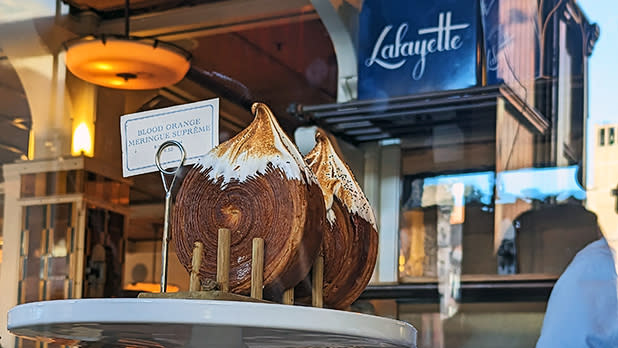 Flaky, decadent croissant-like creation known as a supreme is displayed on a white serving platter in the window of Lafayette Grand Cafe & Bakery