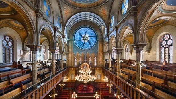 The interior of Eldridge Street Synagogue with a large circular blue glass stained window at the back of the room