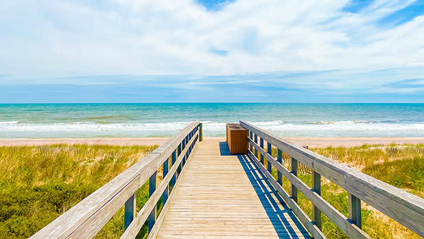 A wooden boardwalk leads directly to the beach, surrounded by natural scenery and inviting ocean views.