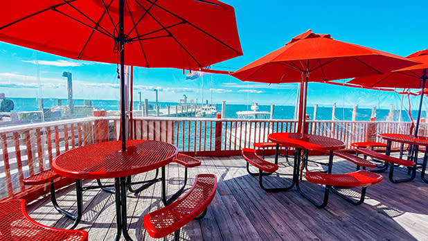 A view of several red tables arranged on a wooden deck overlooking a bay at Cherry's on the Bay in Cherry Grove.