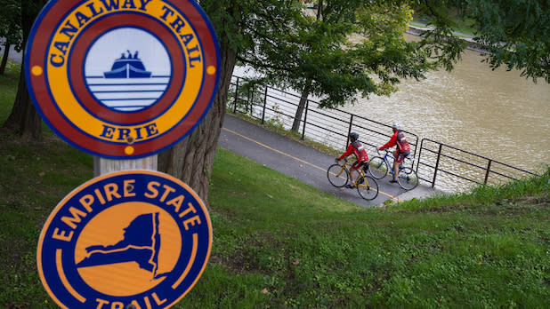 Two people bike along the Erie Canal on the Erie Canalway Trail, part of the Empire State Trail