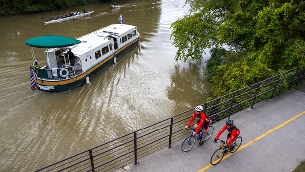 Two people biking along the canal where a tour boat floats by