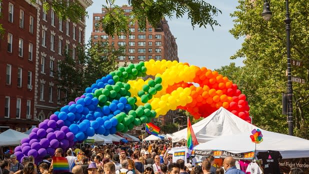 Crowds gather in Greenwich Village under an arch of Pride balloons.