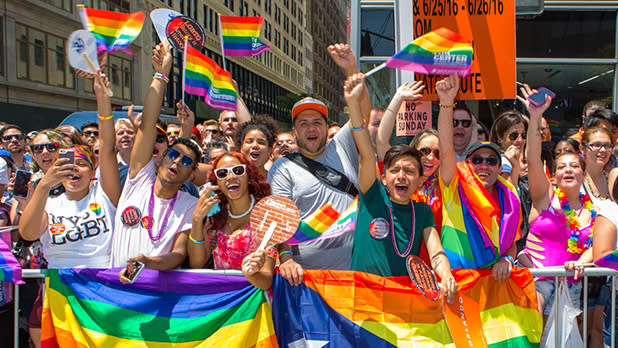 A crowd of people waving rainbow flags and holding a large rainbow banner at Pride Day in New York City