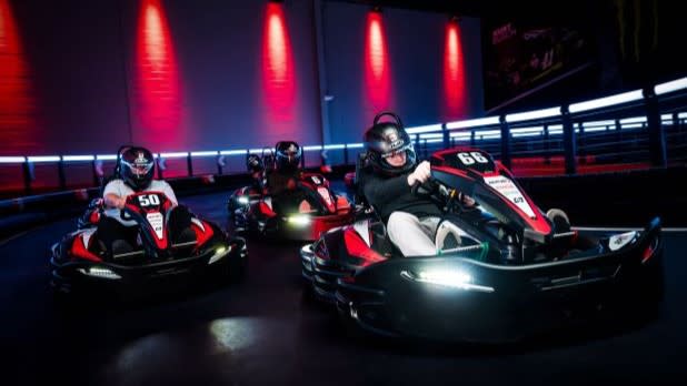 Three go-kart drivers race down an illuminated track at RPM Raceway Long Island