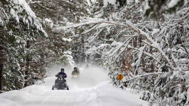 Two snowmobiles drive on the snowy forest path on the Adirondack Rail Trail