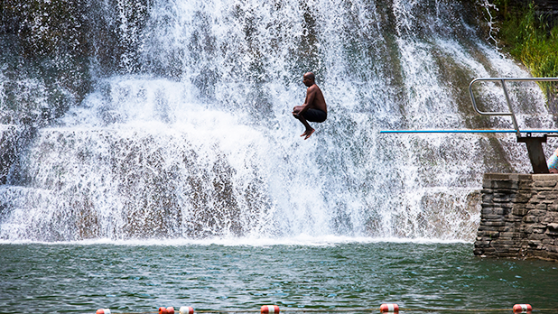 A man does a canonball off a diving board into the swimming hole at Robert H. Treman State Park