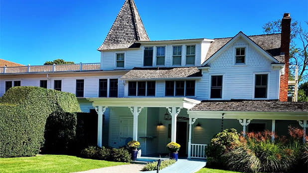 A large white house with a dark brown roof surrounded by green grass