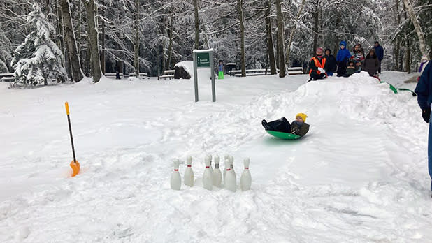 A child in a sled slides down a hill toward bowling pins at Winter Festival in Grafton Lakes State Park