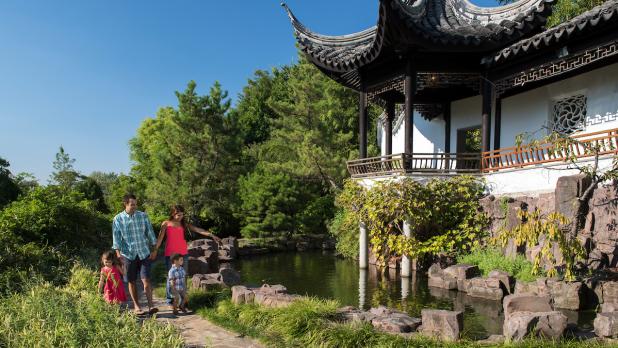 Exterior of a family walking by a building surrounded by green vegetation at the New York Chinese Scholar's Garden at Snug Harbor
