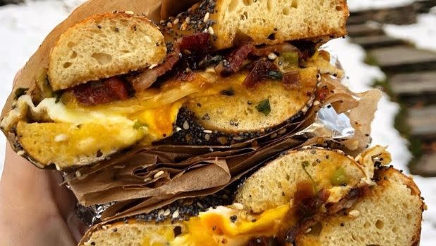 A photo of someone holding an everything bagel  cut in half with bacon, egg and cheese