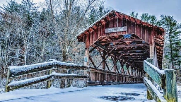 Exterior of a dark brown wooden covered bridge in a snowy forest