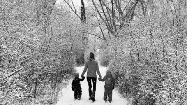 A woman and two young children walk through a snow covered forrest
