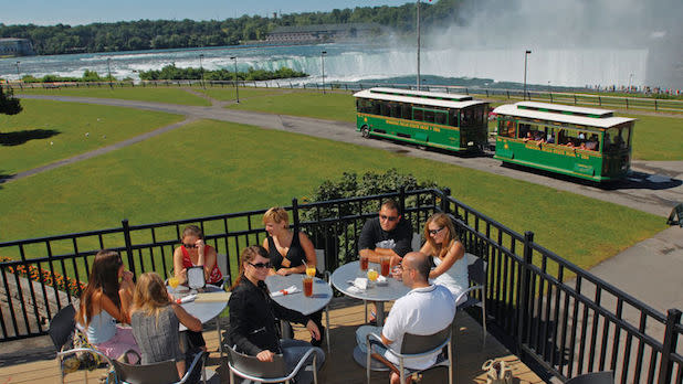 A group of people enjoy a meal from the Top of the Falls outdoor patio looking out at Niagara Falls