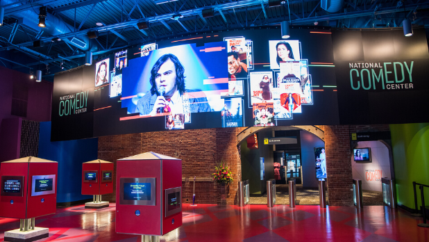 The inside of the National Comedy Center showing various screens of comedians and interactive displays