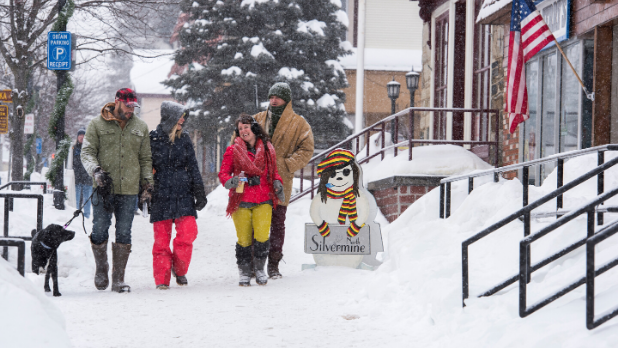 A picture of four people and one dog walking in the snow at the Lake George Winter Carnival