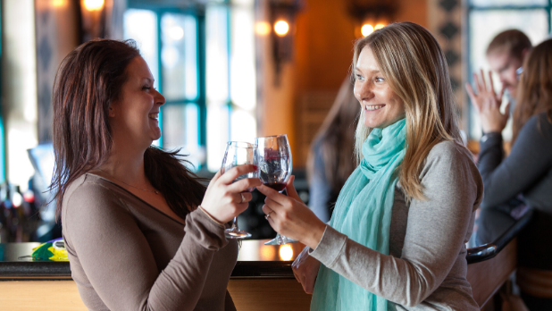 A photo of two ladies clinking wine glasses