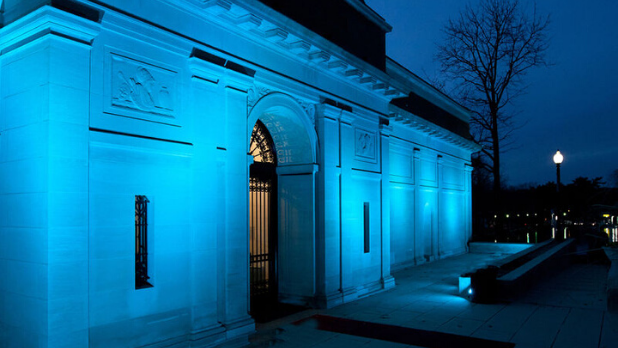 A photo of the exterior of The Heckscher Museum of Art which is lit blue
