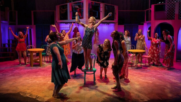 A photo of a girl performing on a chair surrounded by cast mates on stage
