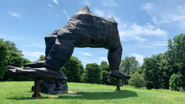 A photo of a three-legged sculpture balancing on a head at the Storm King Art Center