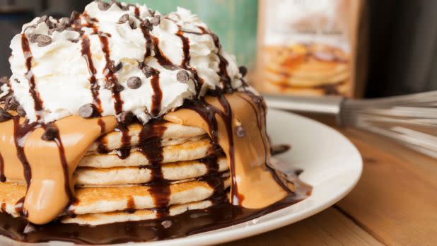 stack of pancakes covered in peanut butter, chocolate syrup, whipped cream