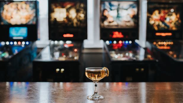 a craft cocktail atop a table with arcade games in the background