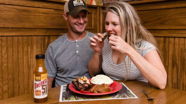 Man and woman excitedly eating plate of BBQ ribs