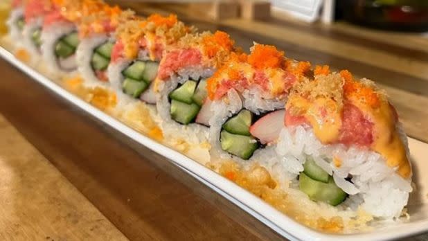 Close-up picture of sushi roll, cucumber and avocado inside, tuna and sauce on outside