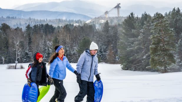 People walking with sleds on snow against backdrop of mountains