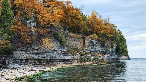 Colorful orange and yellow fall foliage on trees atop a cliff over a lake