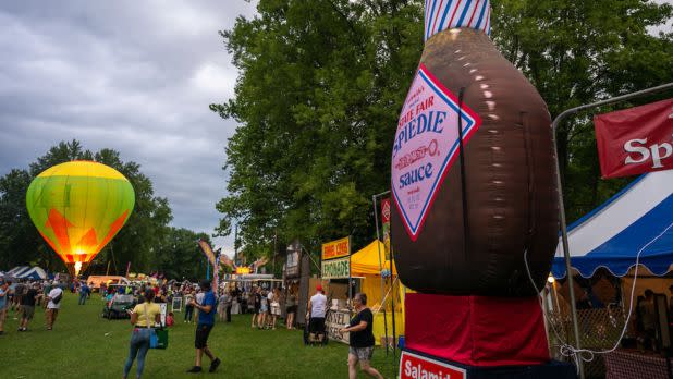 People walking in a field where there is a hot air balloon being inflated and food vendors
