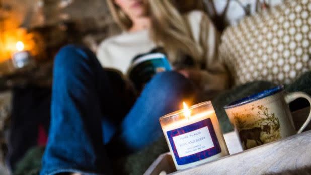 Woman sitting on a couch reading a book with a candle lit in the foreground