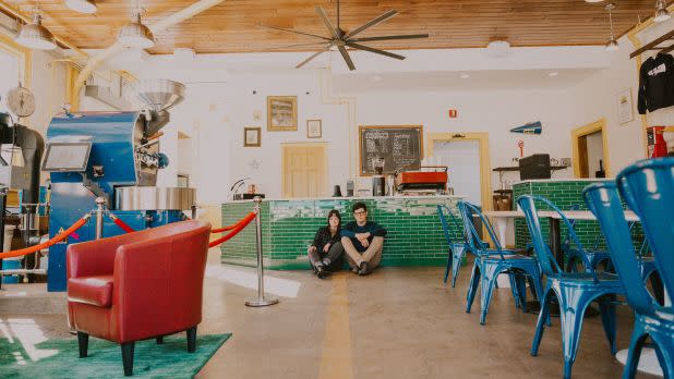 Bright, spacious café with teal chairs and a green-tiled counter. A couple sits on the floor, conveying a relaxed vibe. Industrial decor.