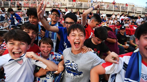 A group of enthusiastic children in soccer jerseys and scarves cheer excitedly at a FIFA World Cup watch party.