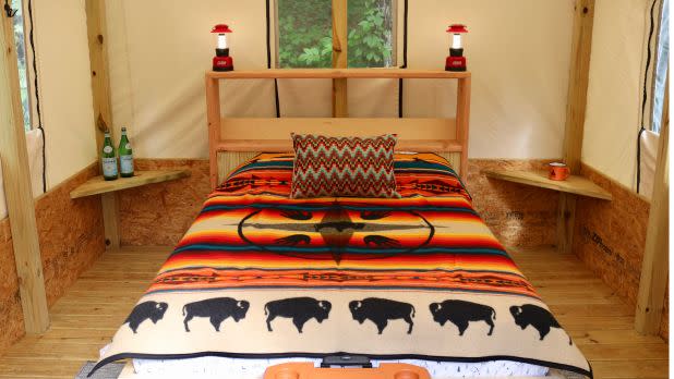 Cozy rustic tent bedroom with a colorful Southwestern blanket, black buffalo motifs, wood bed frame, lanterns, plants, and side tables.