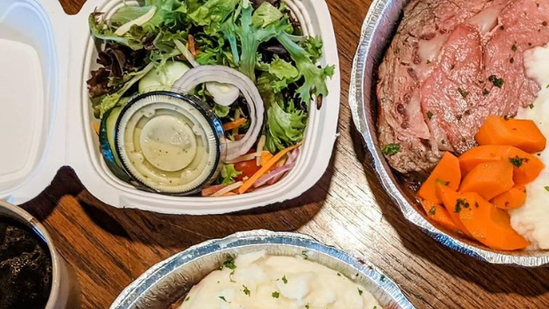 Salad in a takeout container with mashed potatoes, carrots and slow roasted prime rib
