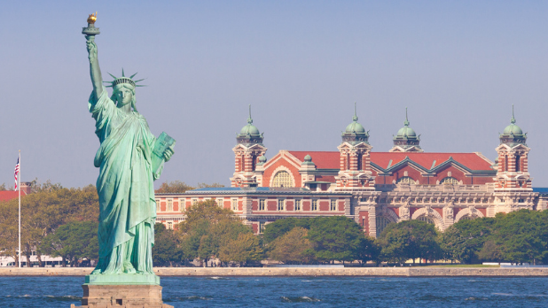 The Statue of Liberty with Ellis Island in the background on a sunny day