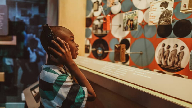 A little boy with headphones on listening to an exhibit at Bethel Woods