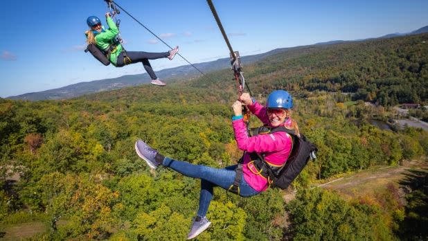 Two people soar over the trees on the Catamount ZipLine