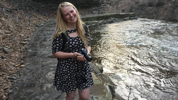 Official I LOVE NY Leaf Peeper, Megan, standing with her camera in front of a gorge in Ithaca