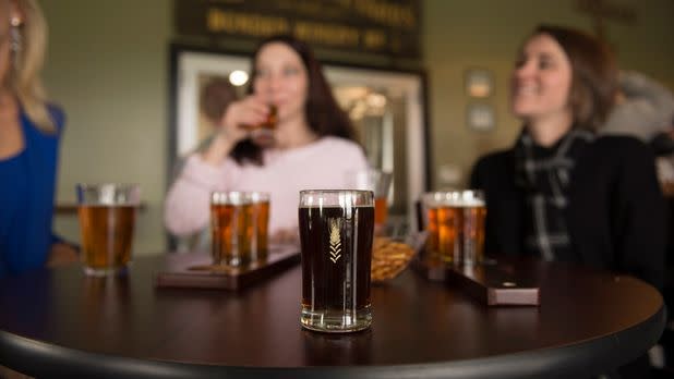 Focused on a beer in a glass on table with three women drinking beers out of focus