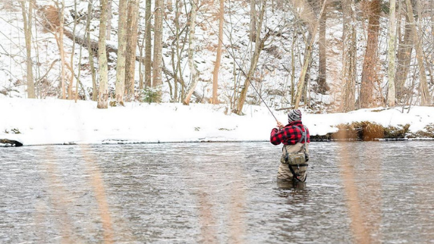 A man fishing in a river during the winter season