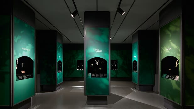 An exhibit with turquoise and light green walls featuring jewels in various shades of green