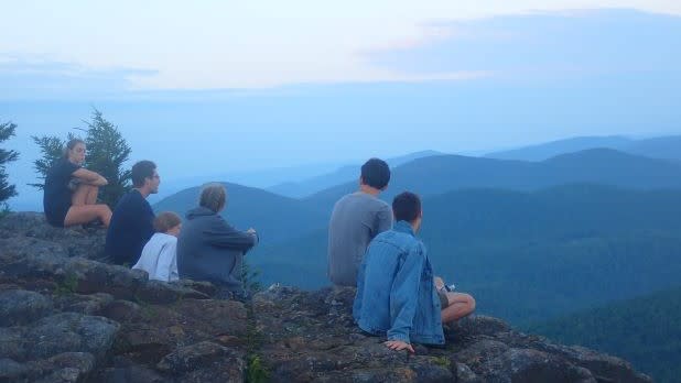 A group of teens gaze out at rolling mountain views from a cliffs edge
