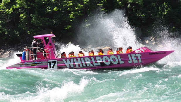 A neon pink whirpool jet boat riding speedily through the Niagara River with several passengers on board